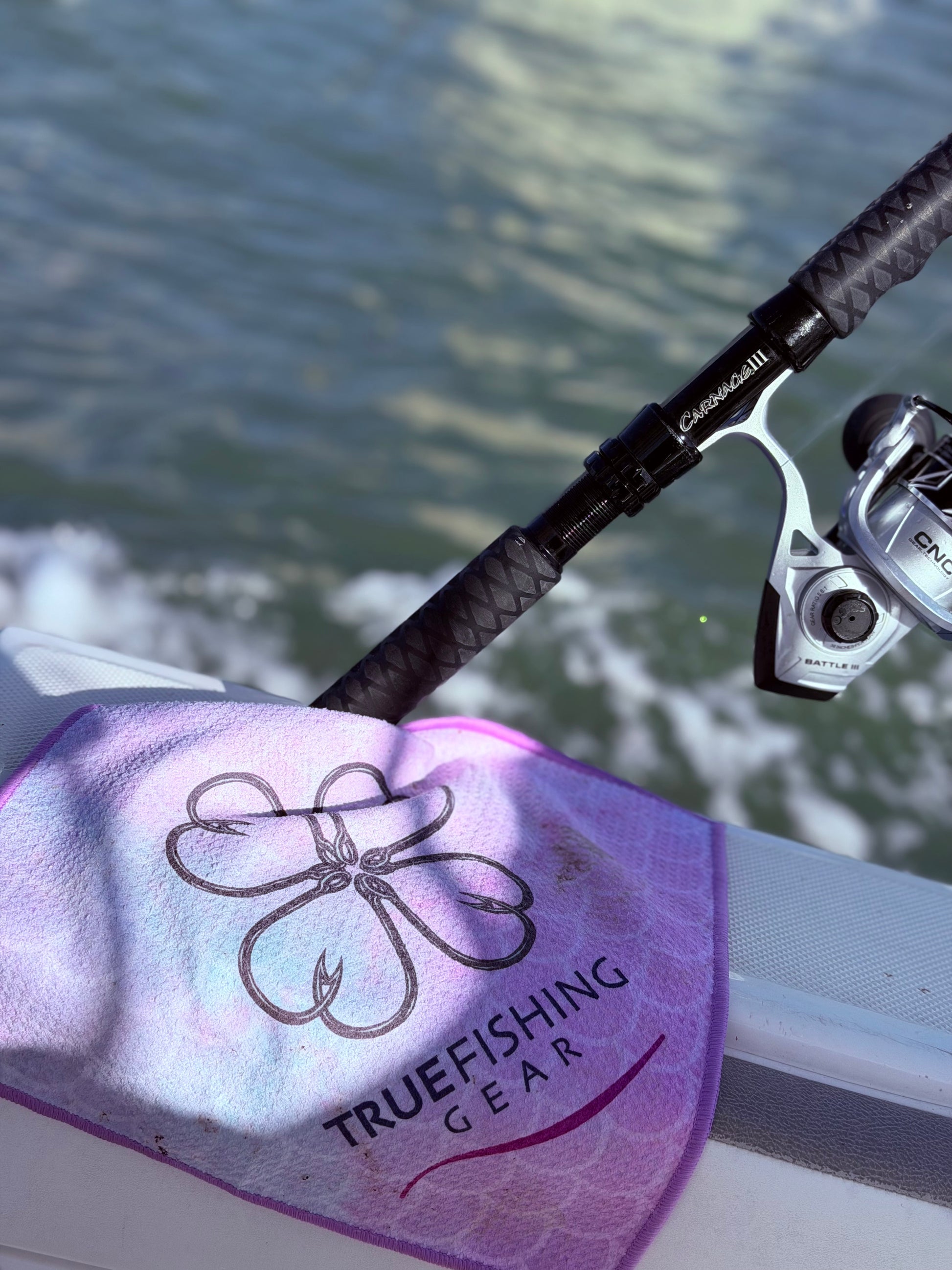 Fishing rod with reel on a purple towel featuring 'True Fishing Gear' logo, water background