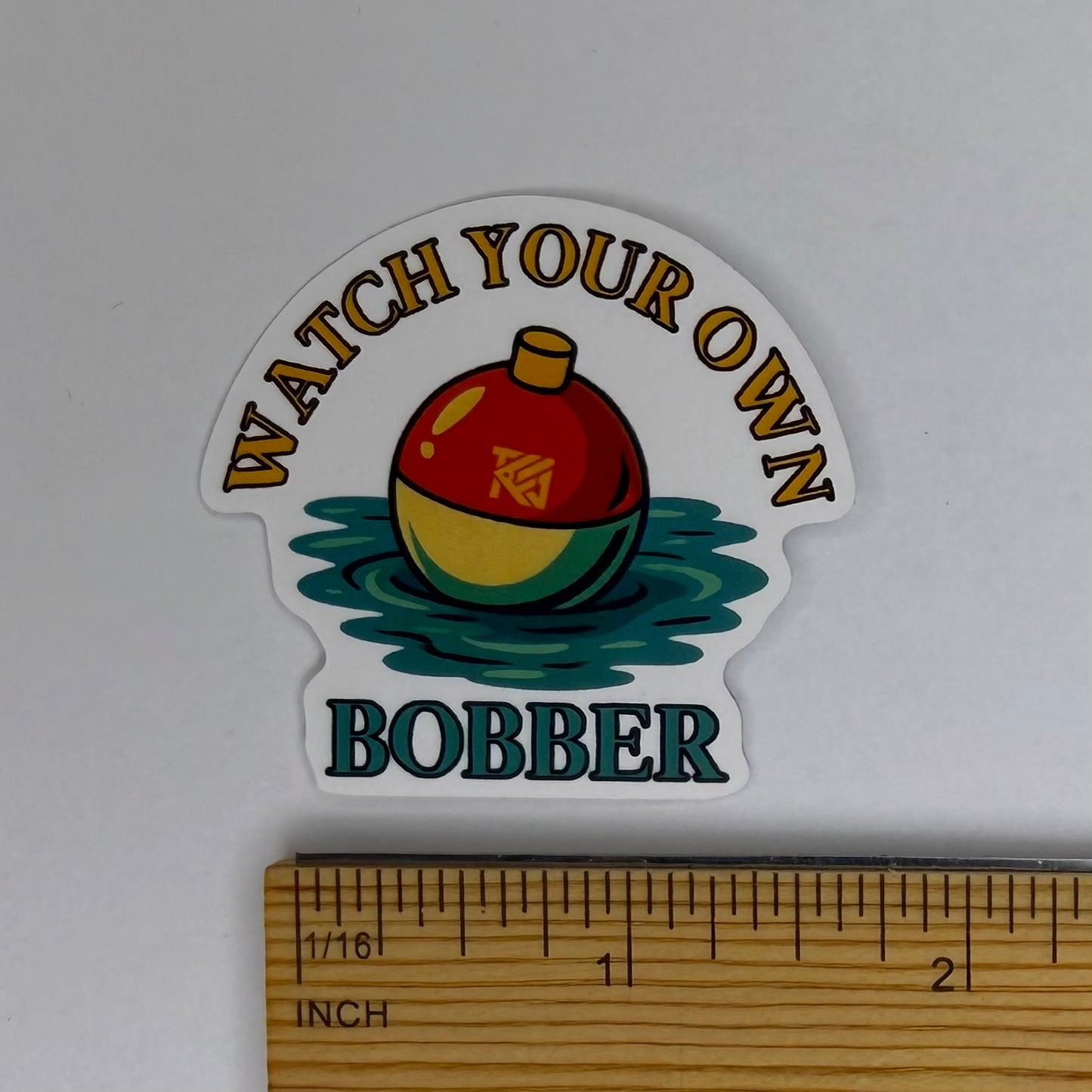 Sticker with a bobber design and text 'Watch Your Own Bobber' next to a ruler for scale.